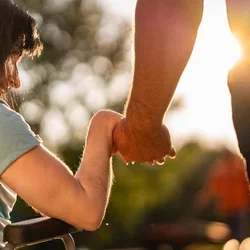 Two people holding hands with the sun in front of them